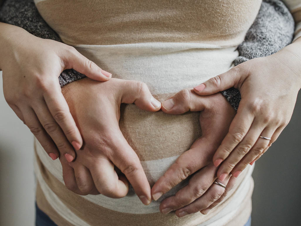 A closeup of a pregnant woman and her partner holding her belly