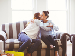 A pregnant woman accepts a gift and hugs the friend giving it to her.