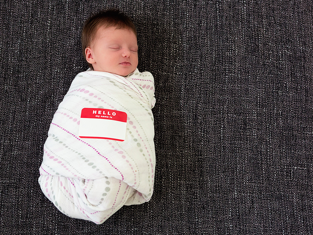 newborn baby in swaddle with sticker 'Hello my name is (blank)'