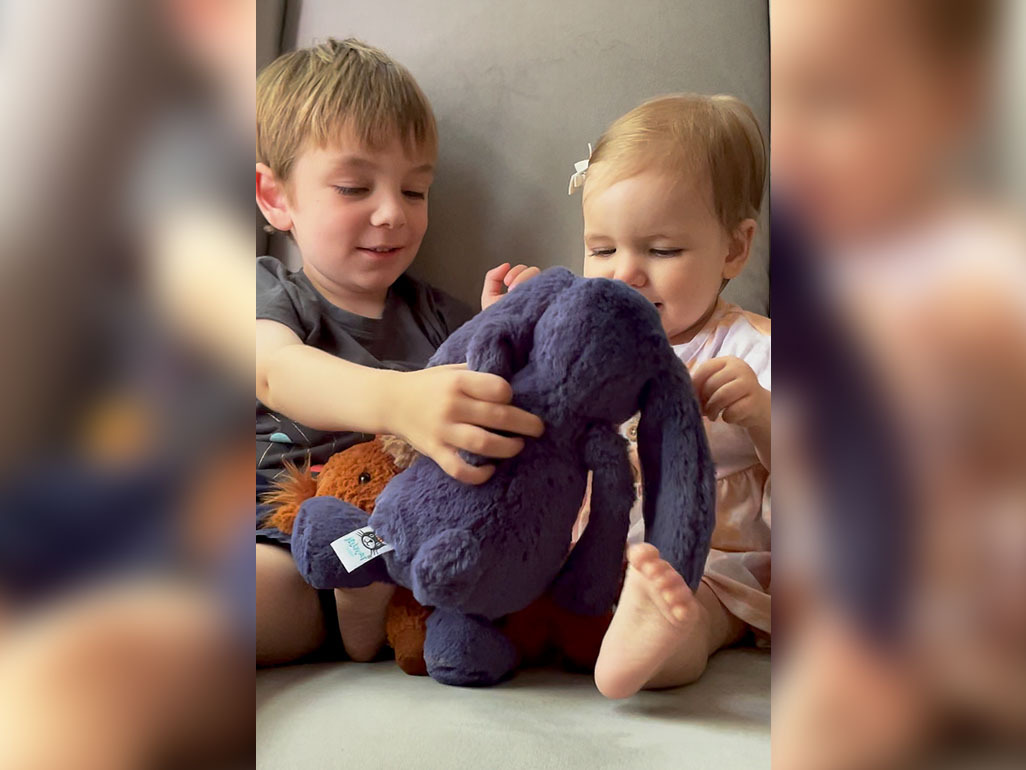 Siblings sitting in a chair, playing with a stuffed bunny