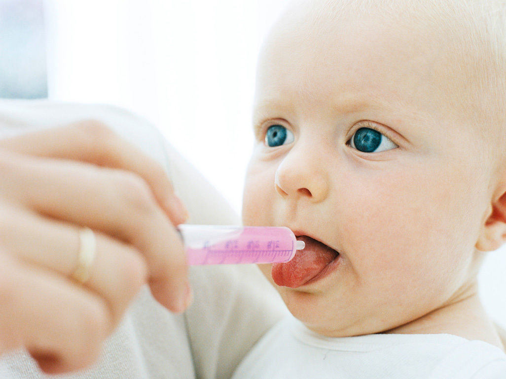 baby getting oral medicine through plastic syringe