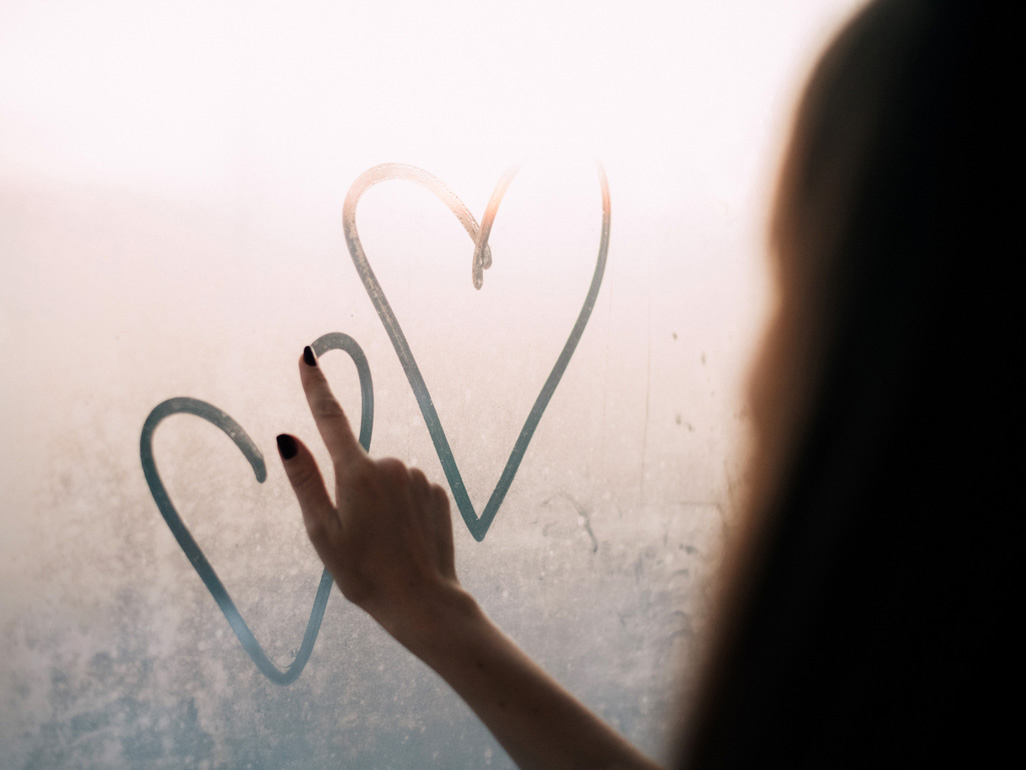 Woman tracing two hearts on window glass
