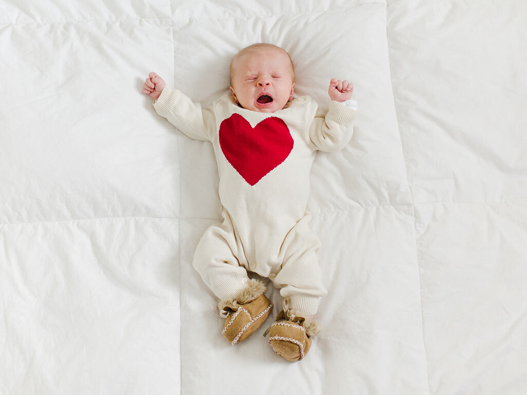 A newborn wearing a white onesie with a red heart on it