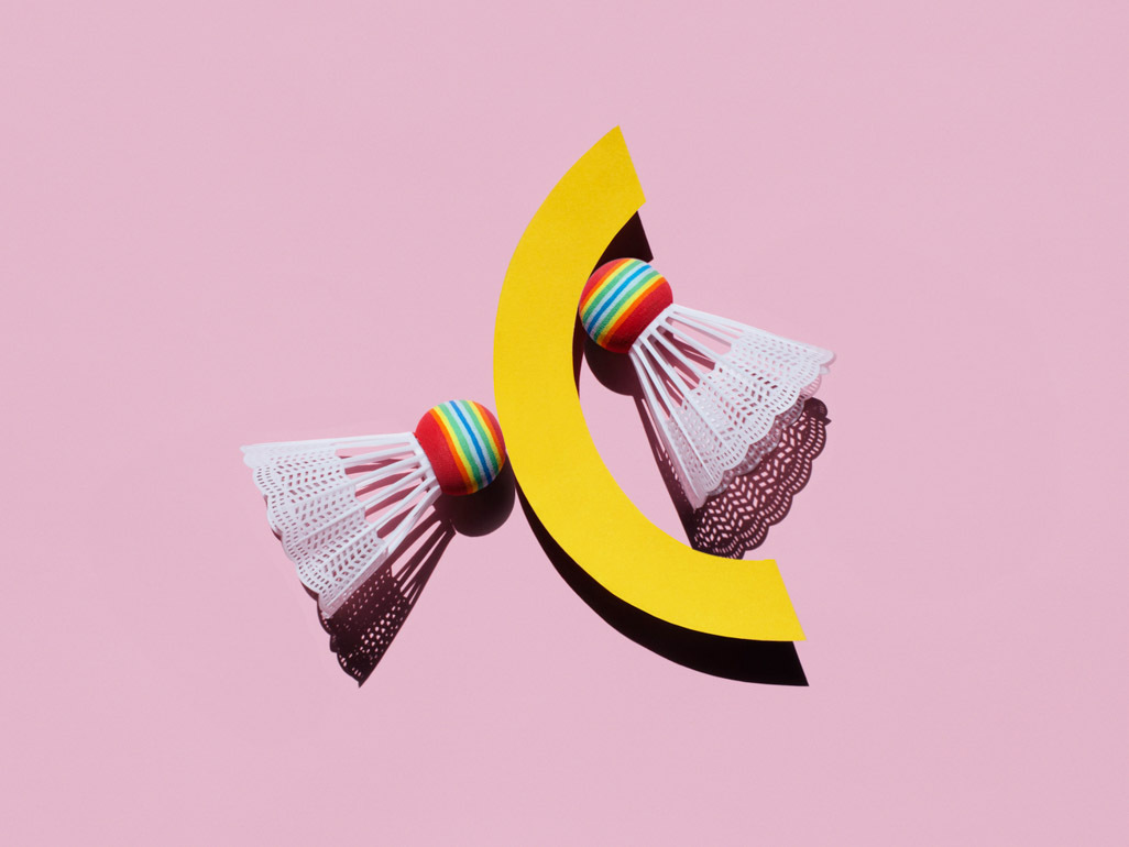 two badminton shuttlecocks next to a yellow crescent shape on a pink background