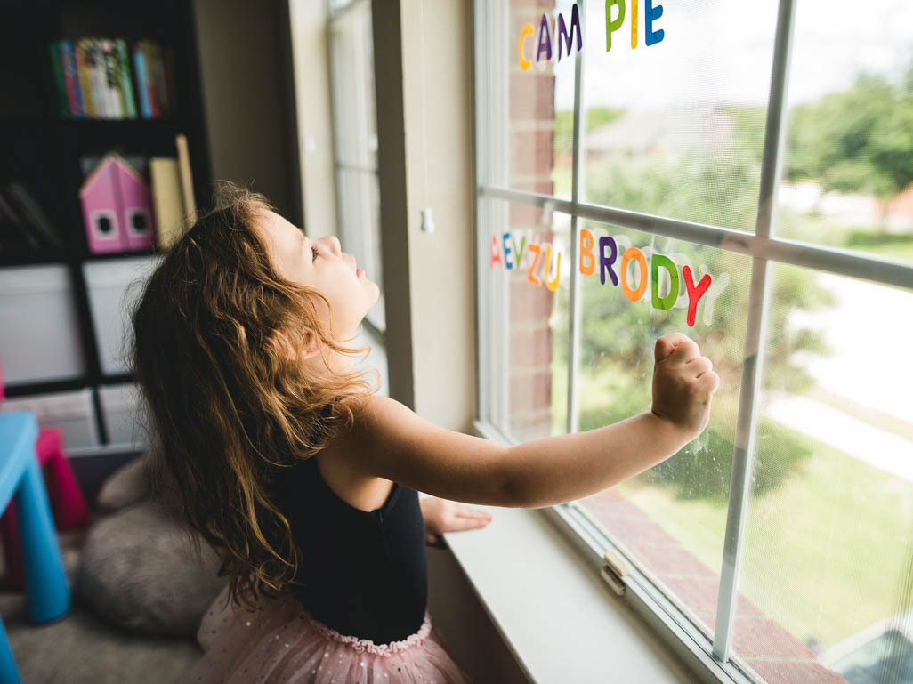A little girl playing with letter stickers on a window
