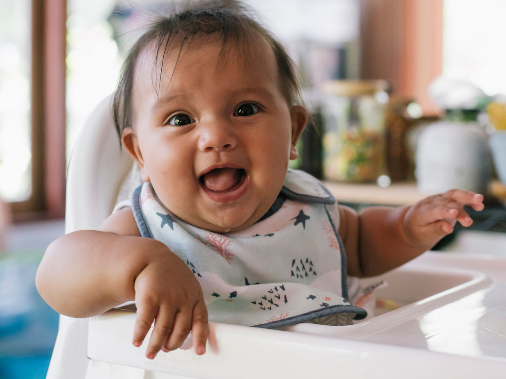 A baby sitting in a highchair, laughing
