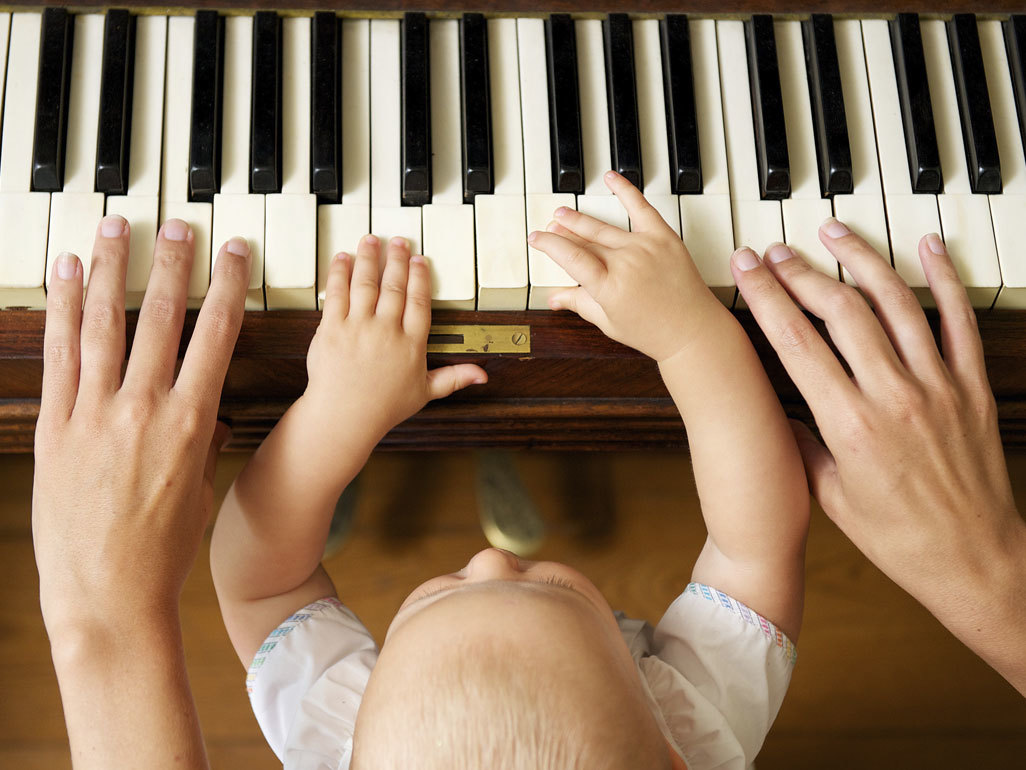 young child sitting with adult while they put their hands on piano keys