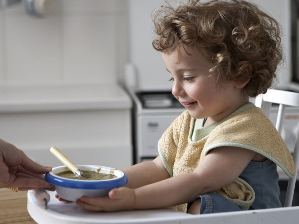 young child in high chair grabbing a bowl of food from adult