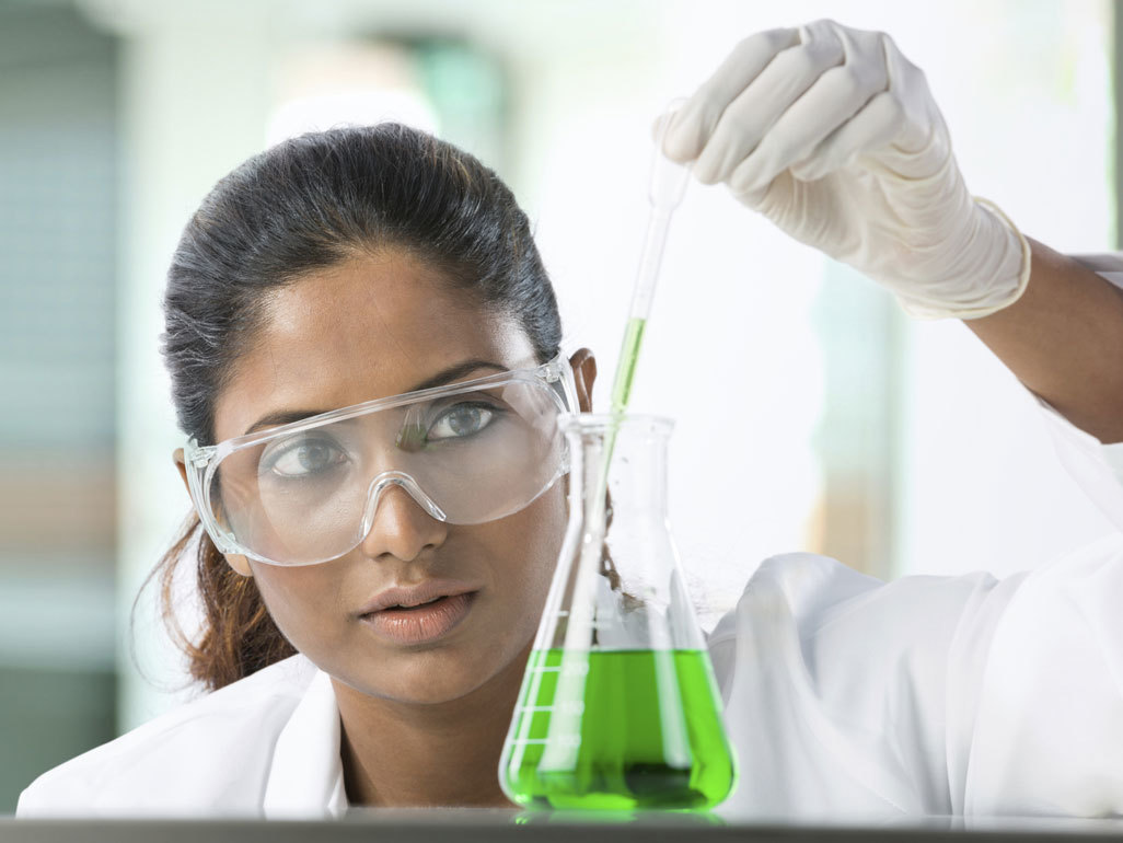 woman scientist wearing safety goggles while putting liquid into a beaker